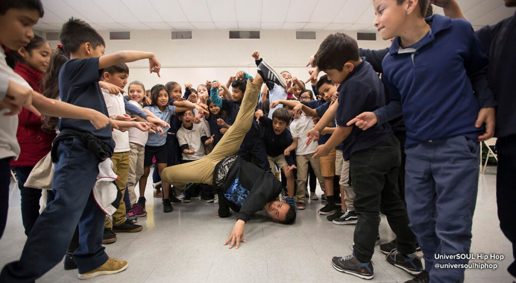 Breakdancer from @universoulhiphop in a breaking freeze, as children in circle point at him.